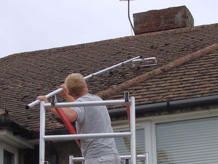 Manually scraping moss off a roof prior to soft washing -  All roof cleaning Services by Roof Repairs Belfast, Northern Ireland
